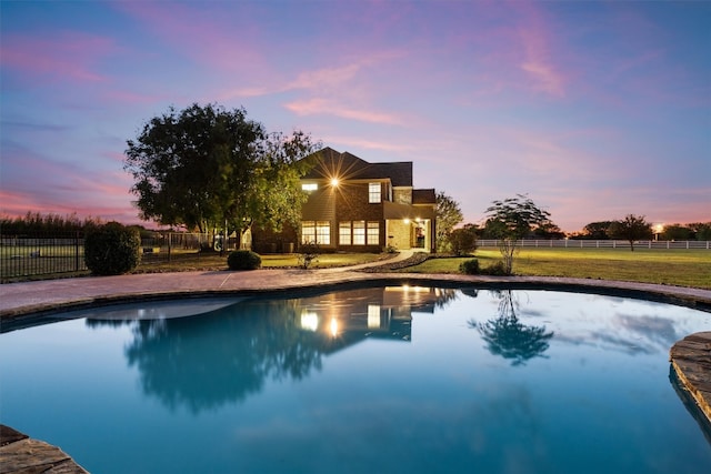 pool at dusk featuring a lawn