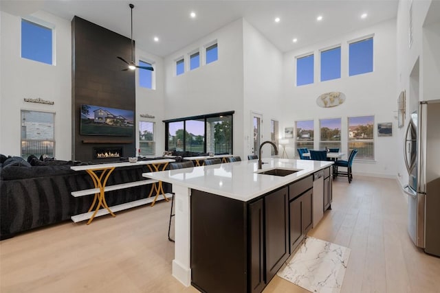 kitchen with ceiling fan, sink, stainless steel appliances, a towering ceiling, and an island with sink