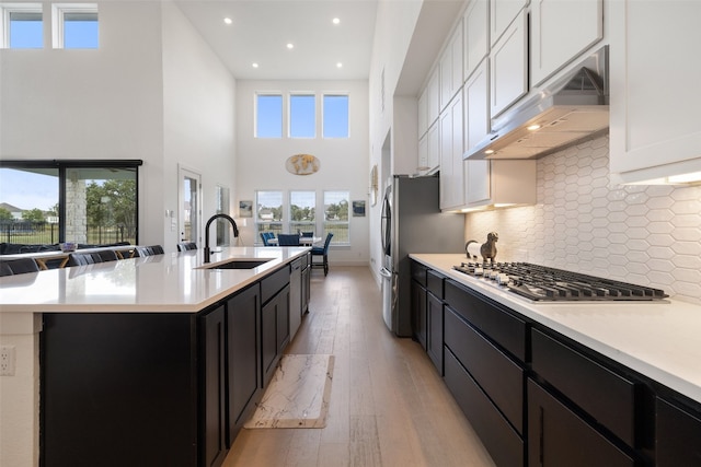 kitchen featuring decorative backsplash, stainless steel appliances, sink, white cabinets, and a high ceiling