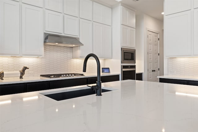 kitchen featuring light stone countertops, appliances with stainless steel finishes, backsplash, and range hood