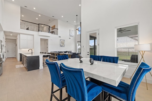 dining area featuring ceiling fan, sink, a towering ceiling, and light hardwood / wood-style flooring