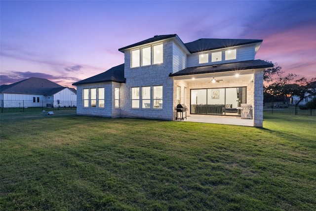 back house at dusk with ceiling fan, a patio area, and a yard