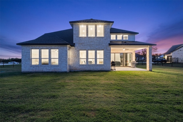 back house at dusk with a lawn, ceiling fan, and a patio area