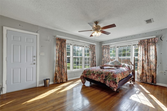 bedroom featuring ceiling fan, wood-type flooring, a textured ceiling, and multiple windows