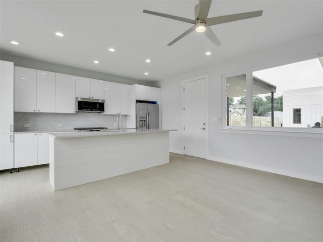 kitchen featuring light wood-type flooring, white cabinets, backsplash, and appliances with stainless steel finishes