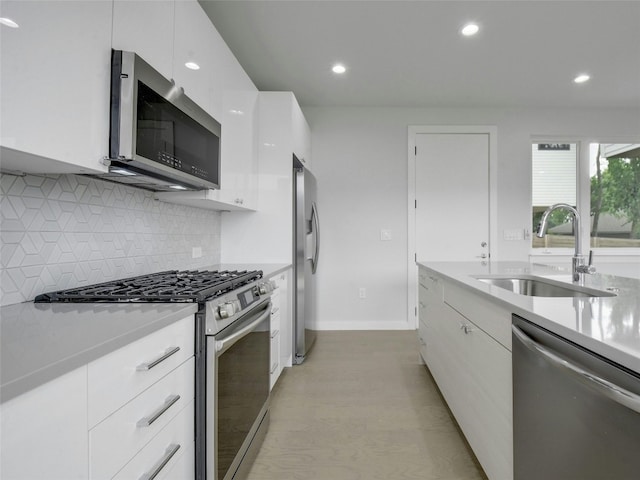kitchen with a sink, modern cabinets, light countertops, white cabinets, and appliances with stainless steel finishes