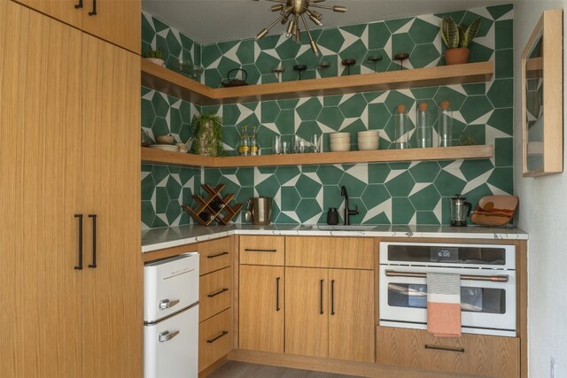 kitchen with backsplash, sink, light brown cabinets, and white appliances