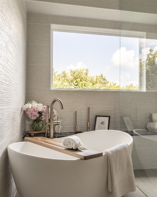 bathroom featuring tile patterned flooring, a tub to relax in, tile walls, and plenty of natural light