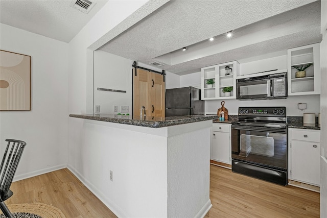 kitchen with kitchen peninsula, black appliances, a barn door, white cabinetry, and light hardwood / wood-style floors