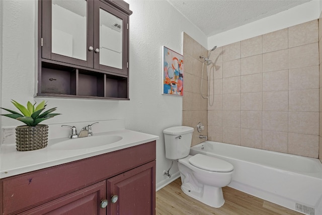 full bathroom with toilet, tiled shower / bath, hardwood / wood-style floors, vanity, and a textured ceiling