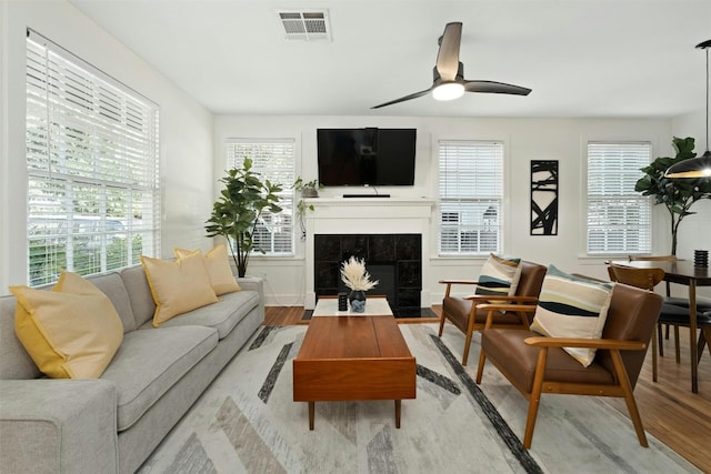 living room with a tile fireplace, ceiling fan, and light hardwood / wood-style floors