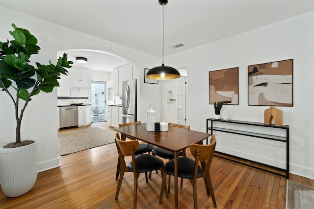 dining space with arched walkways, hardwood / wood-style flooring, visible vents, and baseboards