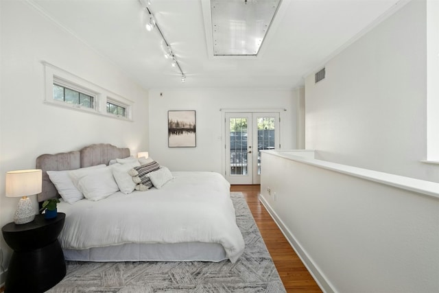 bedroom with wood finished floors, visible vents, baseboards, access to exterior, and track lighting