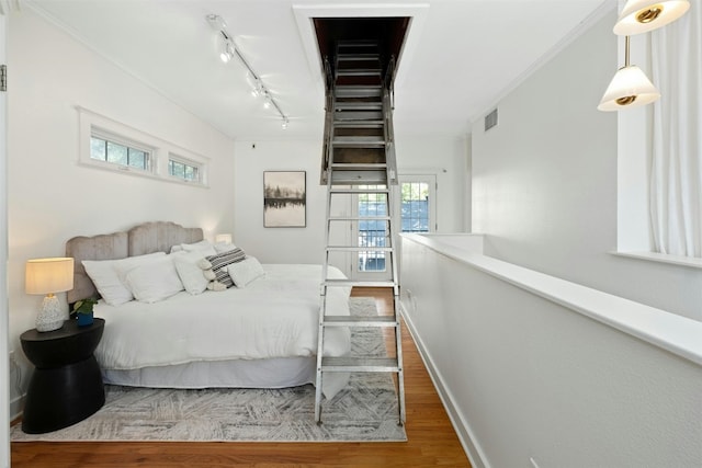 bedroom with baseboards, visible vents, ornamental molding, wood finished floors, and rail lighting