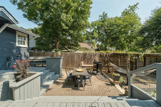 wooden deck with a fenced backyard, outdoor dining area, a patio, and area for grilling