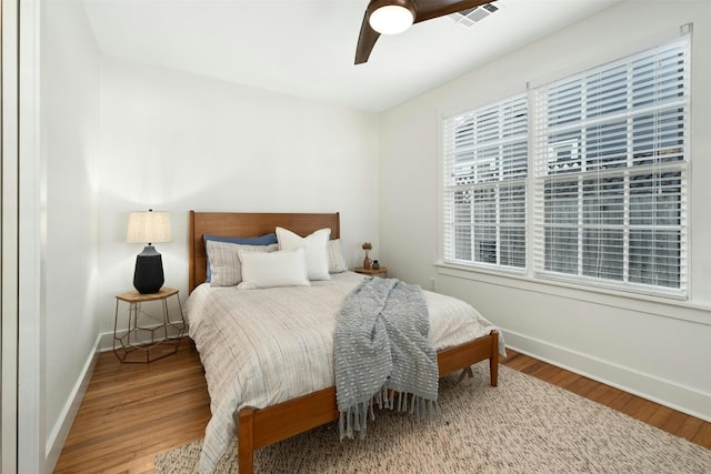 bedroom featuring a ceiling fan, wood finished floors, visible vents, and baseboards