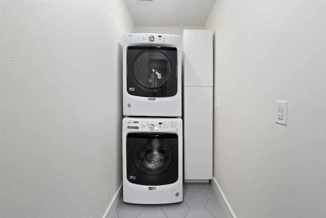 laundry area with light tile patterned floors, stacked washer and dryer, laundry area, and baseboards