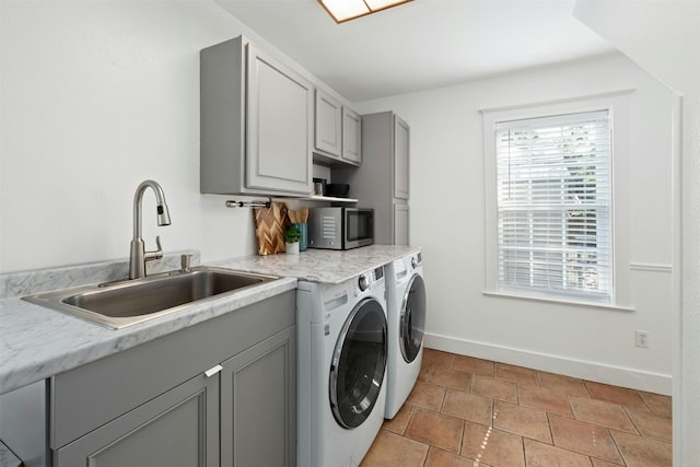 clothes washing area featuring baseboards, a sink, cabinet space, and washer and dryer