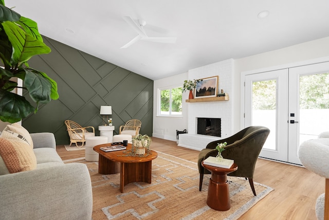 living room featuring a healthy amount of sunlight, light hardwood / wood-style flooring, french doors, and a brick fireplace