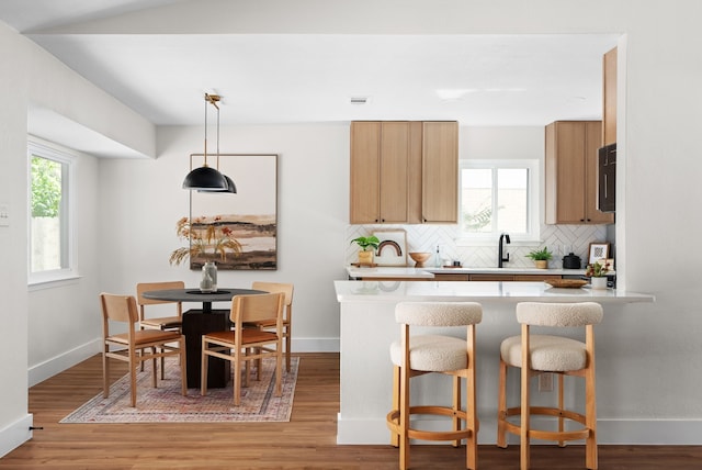 kitchen featuring a breakfast bar area, hanging light fixtures, sink, light hardwood / wood-style flooring, and backsplash