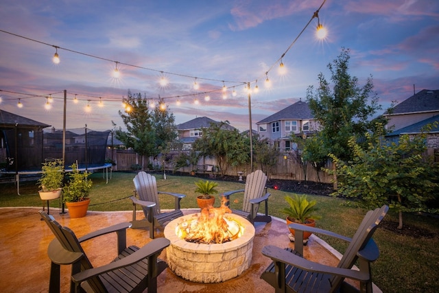 patio terrace at dusk with a trampoline, an outdoor fire pit, and a lawn