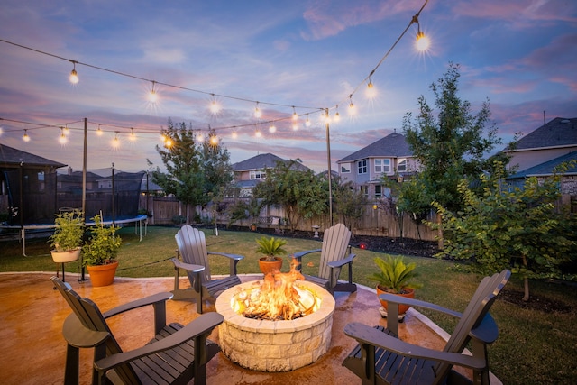 patio terrace at dusk featuring an outdoor fire pit, a trampoline, and a yard