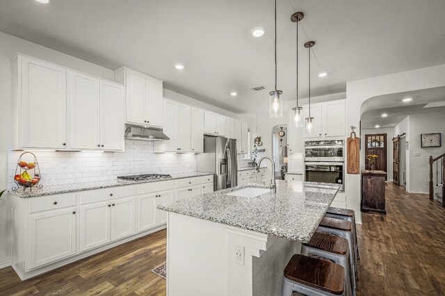 kitchen with pendant lighting, white cabinets, stainless steel appliances, an island with sink, and sink