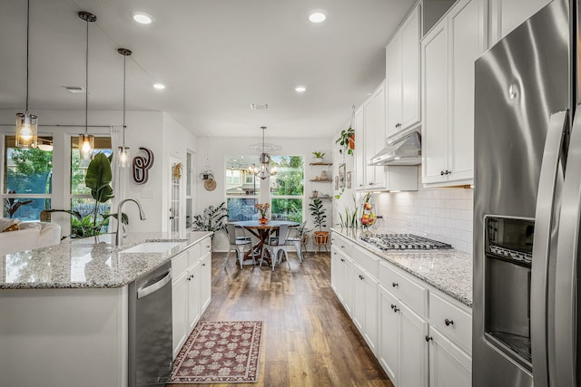 kitchen with appliances with stainless steel finishes, white cabinetry, sink, hanging light fixtures, and a center island with sink