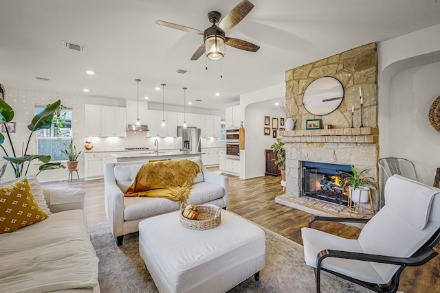 living room with ceiling fan, sink, wood-type flooring, and a fireplace