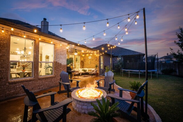 patio terrace at dusk featuring an outdoor fire pit, a lawn, and a trampoline