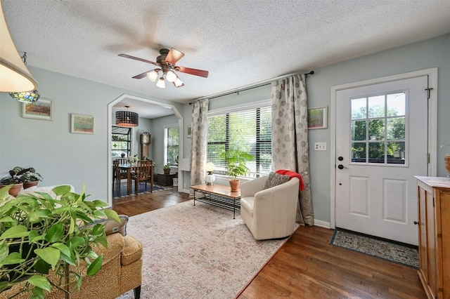 living room featuring ceiling fan, a textured ceiling, a wealth of natural light, and dark wood-type flooring