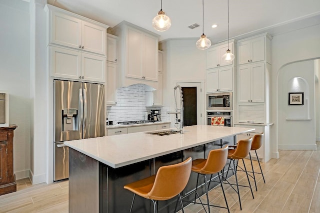 kitchen featuring decorative light fixtures, an island with sink, stainless steel appliances, and white cabinetry