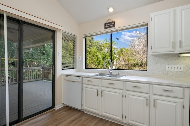 kitchen featuring a sink, lofted ceiling, light wood finished floors, light countertops, and white dishwasher