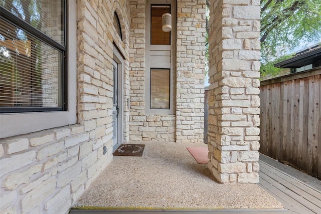 view of exterior entry featuring fence and stone siding