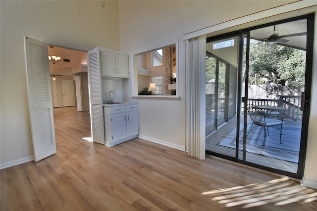 doorway with light wood-style flooring, baseboards, a sink, and ceiling fan with notable chandelier