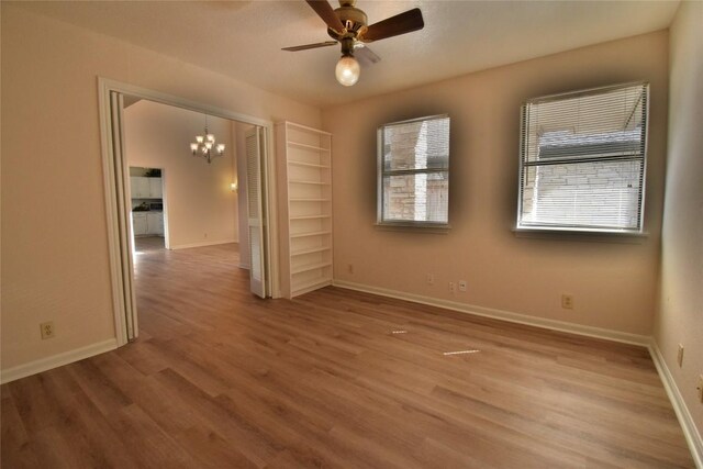 unfurnished room with ceiling fan with notable chandelier, wood-type flooring, and a healthy amount of sunlight