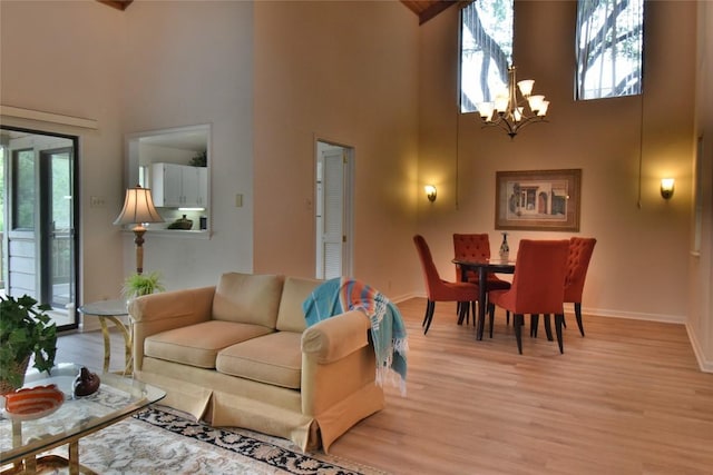 living area with baseboards, a notable chandelier, light wood-style floors, and a towering ceiling