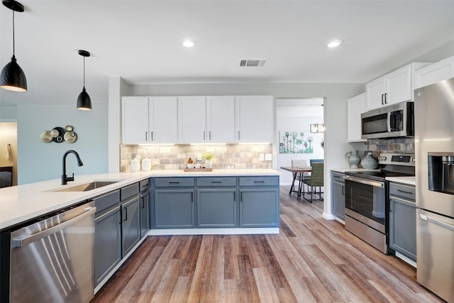 kitchen with white cabinets, hanging light fixtures, sink, appliances with stainless steel finishes, and light wood-type flooring