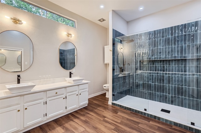 bathroom with hardwood / wood-style floors, vanity, toilet, and tiled shower