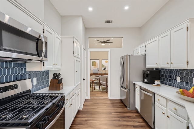 kitchen featuring dark wood-type flooring, white cabinets, decorative backsplash, ceiling fan, and stainless steel appliances