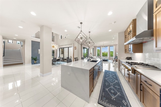 kitchen with light tile patterned floors, a center island with sink, hanging light fixtures, and wall chimney range hood