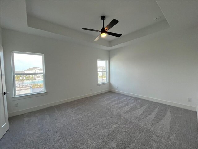 carpeted spare room featuring ceiling fan and a raised ceiling