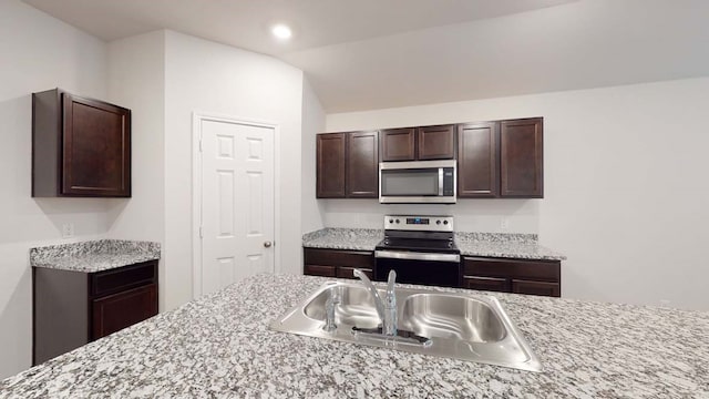 kitchen with appliances with stainless steel finishes, lofted ceiling, dark brown cabinets, and sink