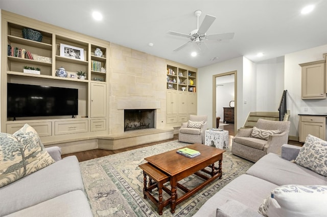 living area featuring a ceiling fan, a tile fireplace, stairway, wood finished floors, and built in shelves