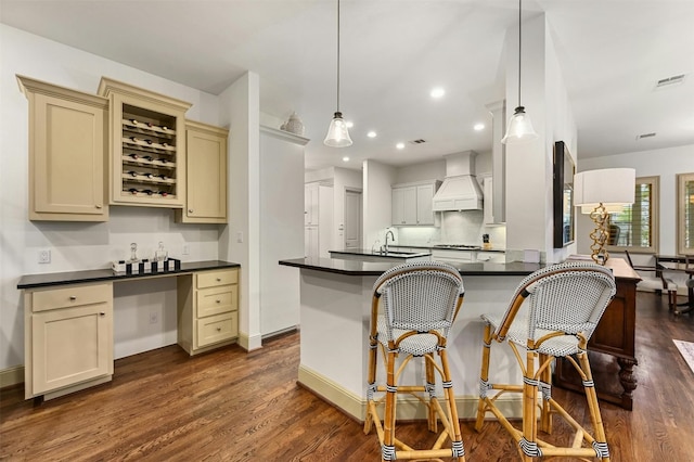 kitchen featuring pendant lighting, kitchen peninsula, cream cabinetry, dark hardwood / wood-style floors, and custom range hood