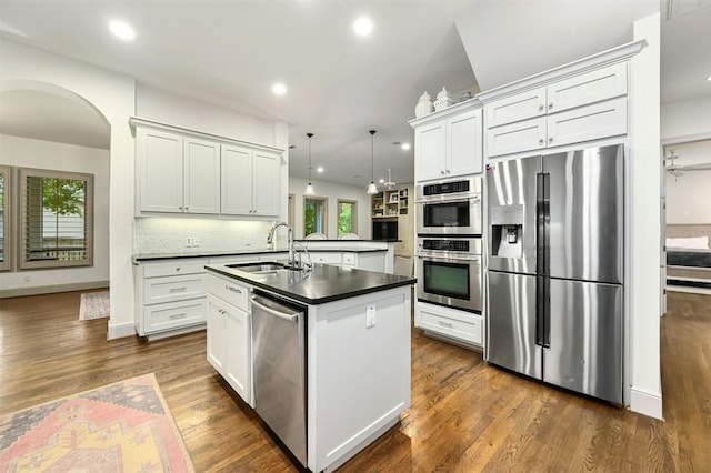 kitchen with dark wood-type flooring, a sink, appliances with stainless steel finishes, an island with sink, and dark countertops