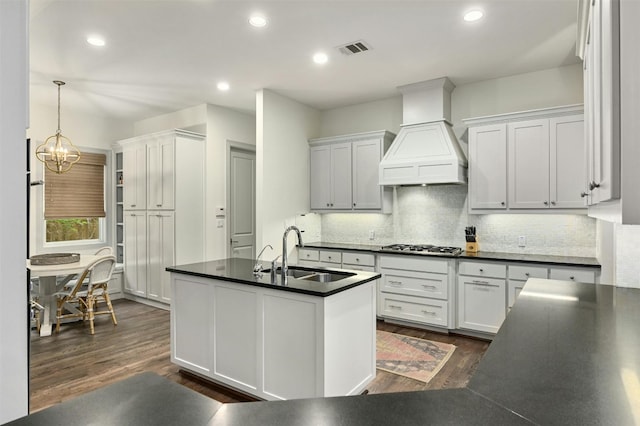 kitchen featuring dark countertops, decorative backsplash, dark wood-type flooring, a sink, and premium range hood