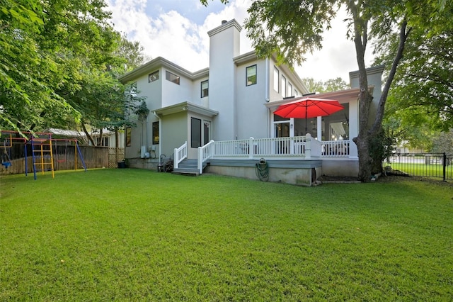 back of house with a playground, fence, a yard, stucco siding, and a chimney