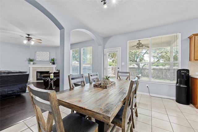 dining room featuring a tile fireplace, light tile patterned flooring, and ceiling fan