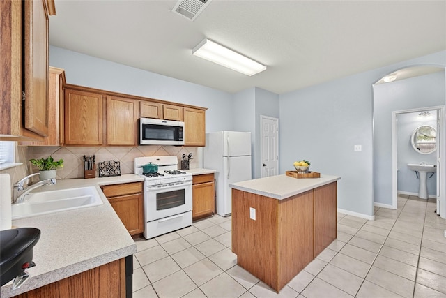 kitchen featuring light tile patterned flooring, sink, white appliances, a kitchen island, and backsplash